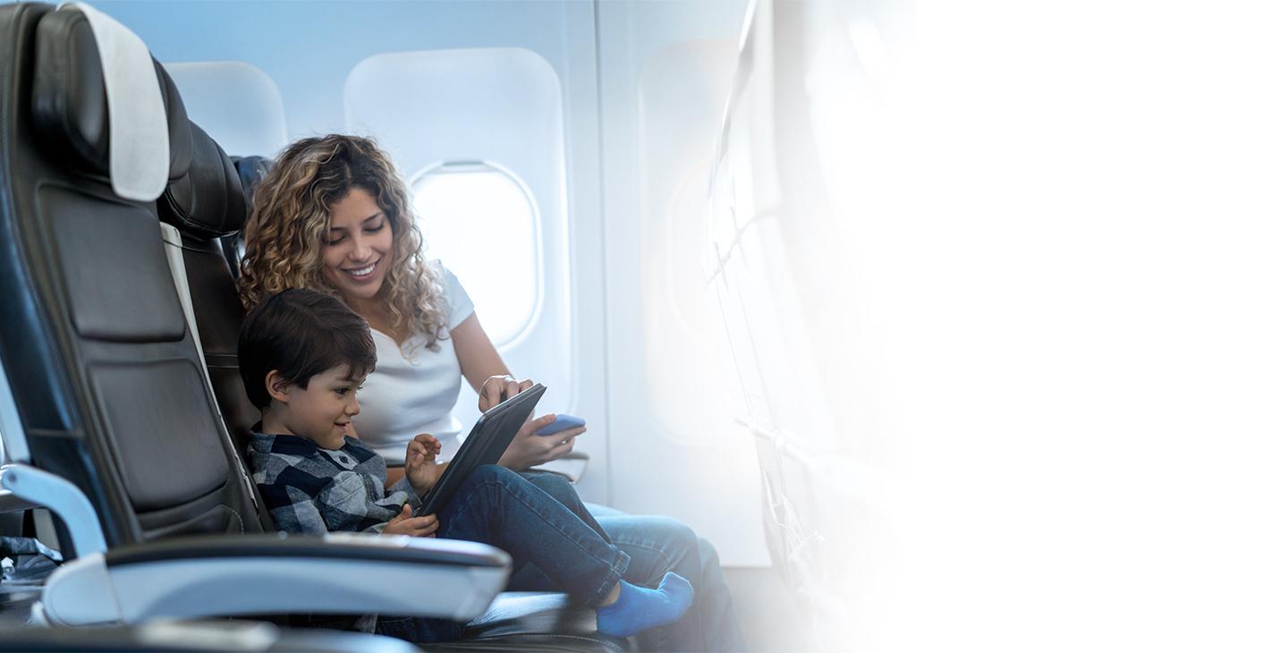 在飞机上，坐在儿子旁边的一位女士正在帮助儿子将平板电脑连接到飞机上的wifi